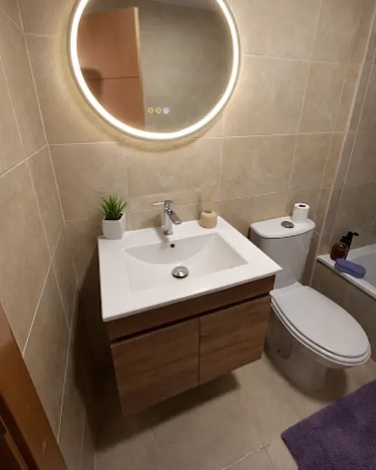 Aseo con mueble de lavabo y espejo circular retroiluminado